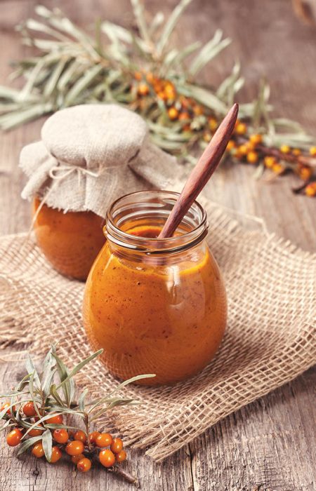 glass jar with sea buckthorn jam on a wooden background (toning, vintage)