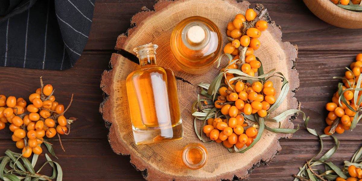 Natural sea buckthorn oil and fresh berries on wooden table, flat lay